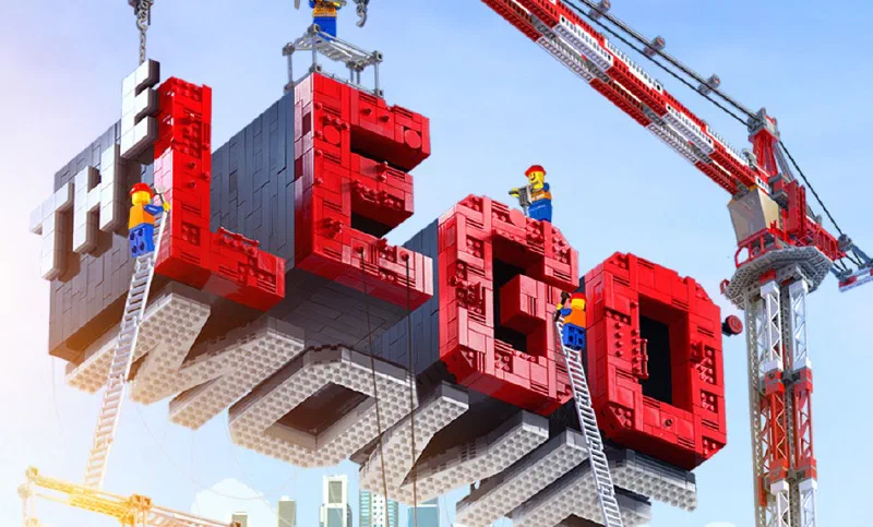 Promotional art for The Lego Movie: the title built from giant red and grey Lego bricks, with minifigure construction workers assembling it from ladders and cranes.