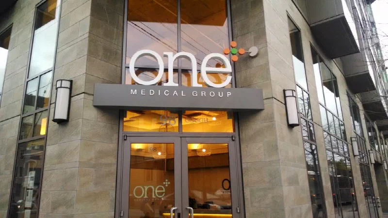 The corner entrance of a One Medical Group clinic, its lit sign mounted above glass doors.