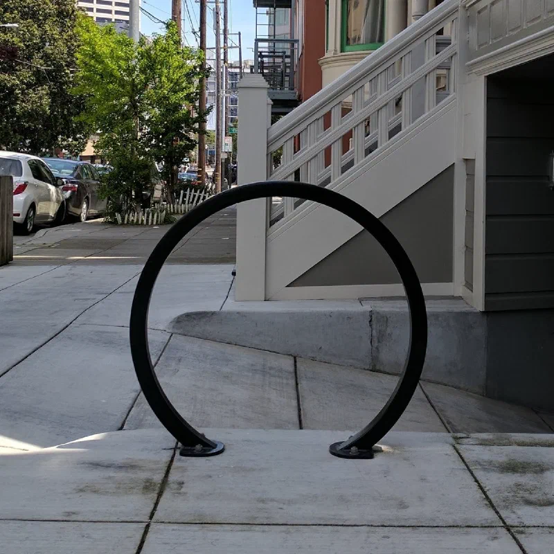 A black circular bike rack bolted into the sidewalk outside a house, beside the front steps.